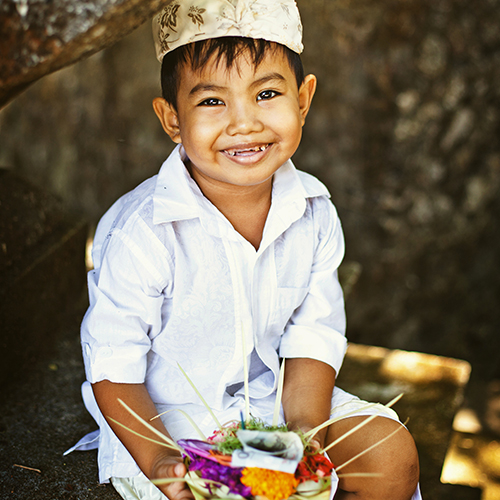 Petit garçon souriant avec une couronne et tenant un plat de fruits